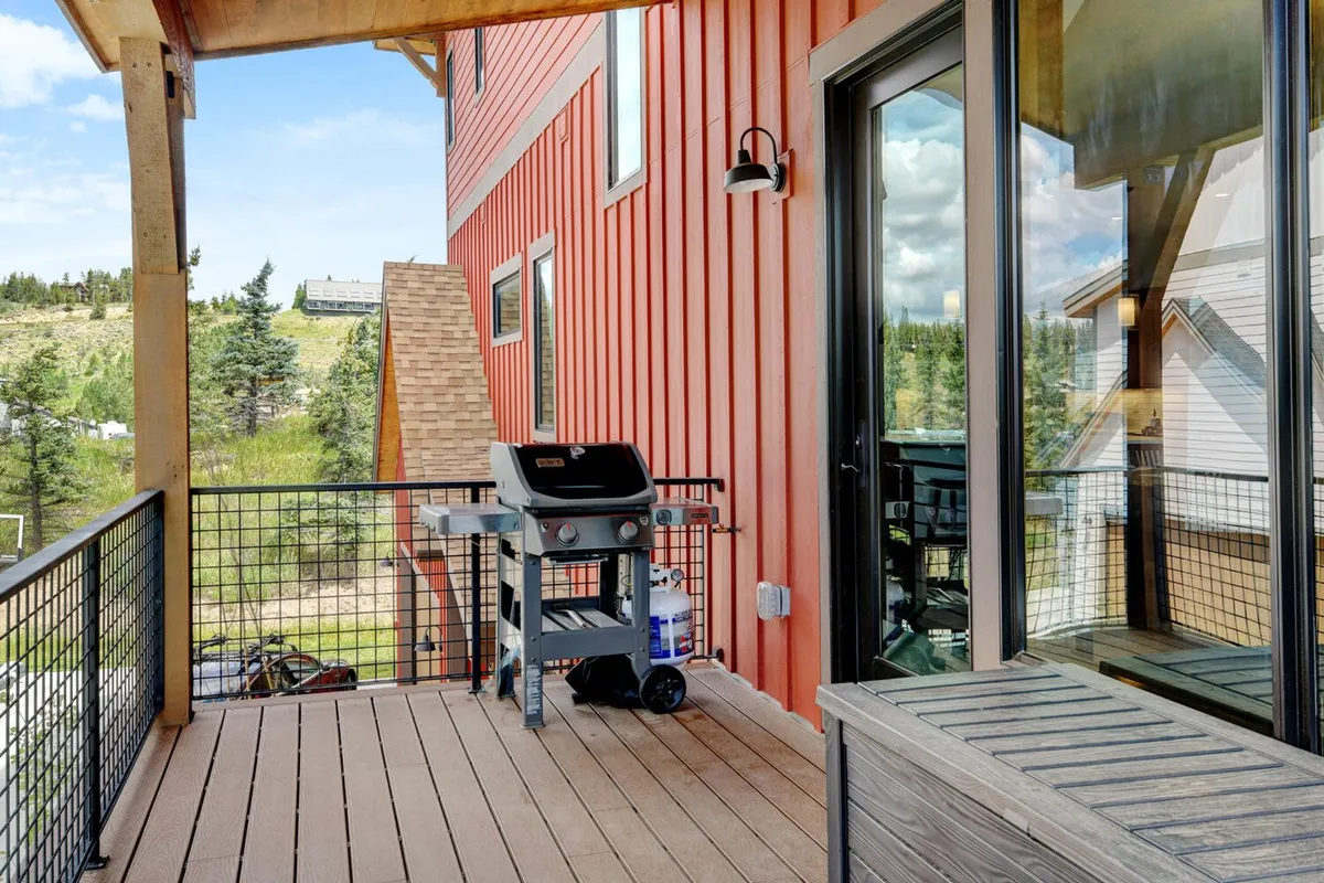 A wooden deck set among trees, featuring a modern BBQ grill and space for outdoor dining or lounging. The casual and welcoming mood invites guests to gather and enjoy meals outside, especially during sunset or under the stars.