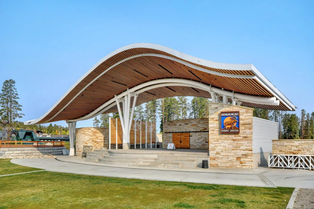 The outdoor stage and amphitheater at Hideaway Park are shown here, featuring a curved roof structure, stone walls, and an open area designed for concerts and community events. The setting is festive and lively, evoking the fun atmosphere of live music and gatherings highlighted in the section content.