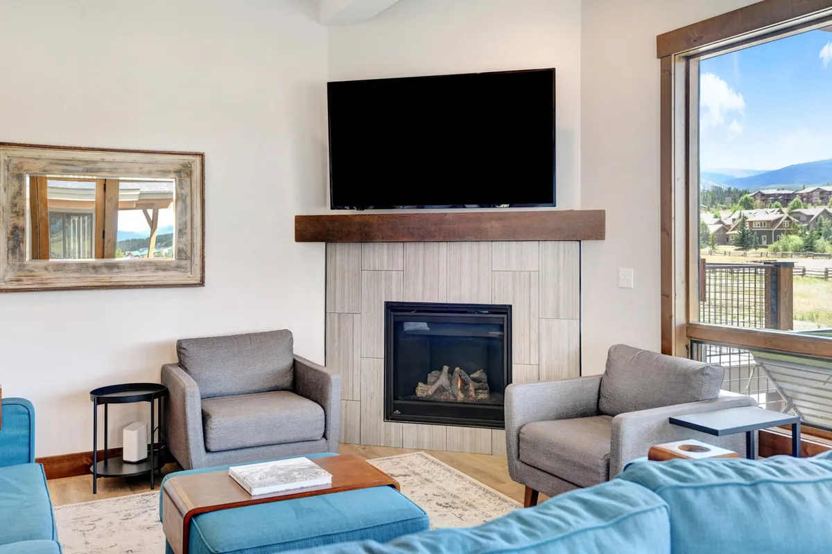 A welcoming main lounge with a fireplace, TV, ample seating, and a view out the window. The arrangement encourages relaxation, connection, and togetherness, offering a comfortable place for adults to gather, converse, or enjoy a group activity.