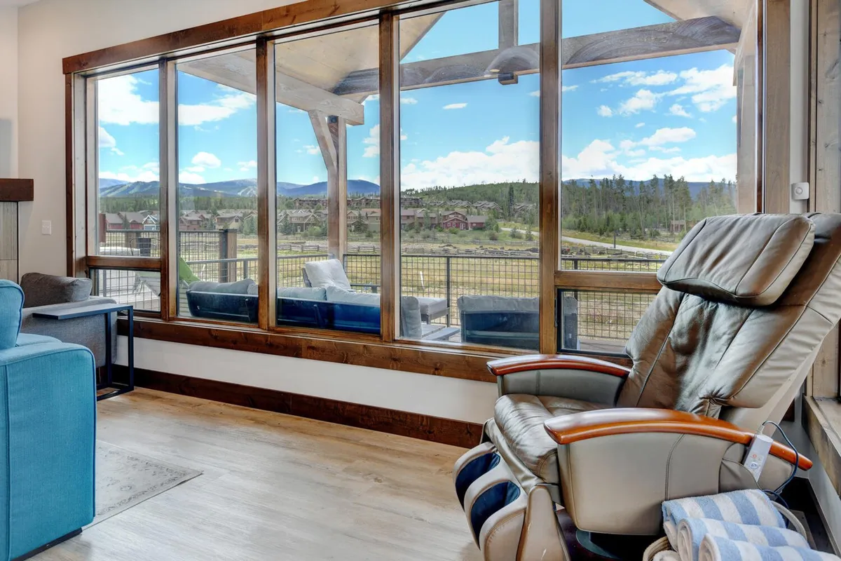 A serene interior living area with large windows offering breathtaking mountain views. Comfortable seating, including a recliner, is arranged to take in the scenery—ideal for relaxing, reading, or simply enjoying the peaceful surroundings after a productive work session.