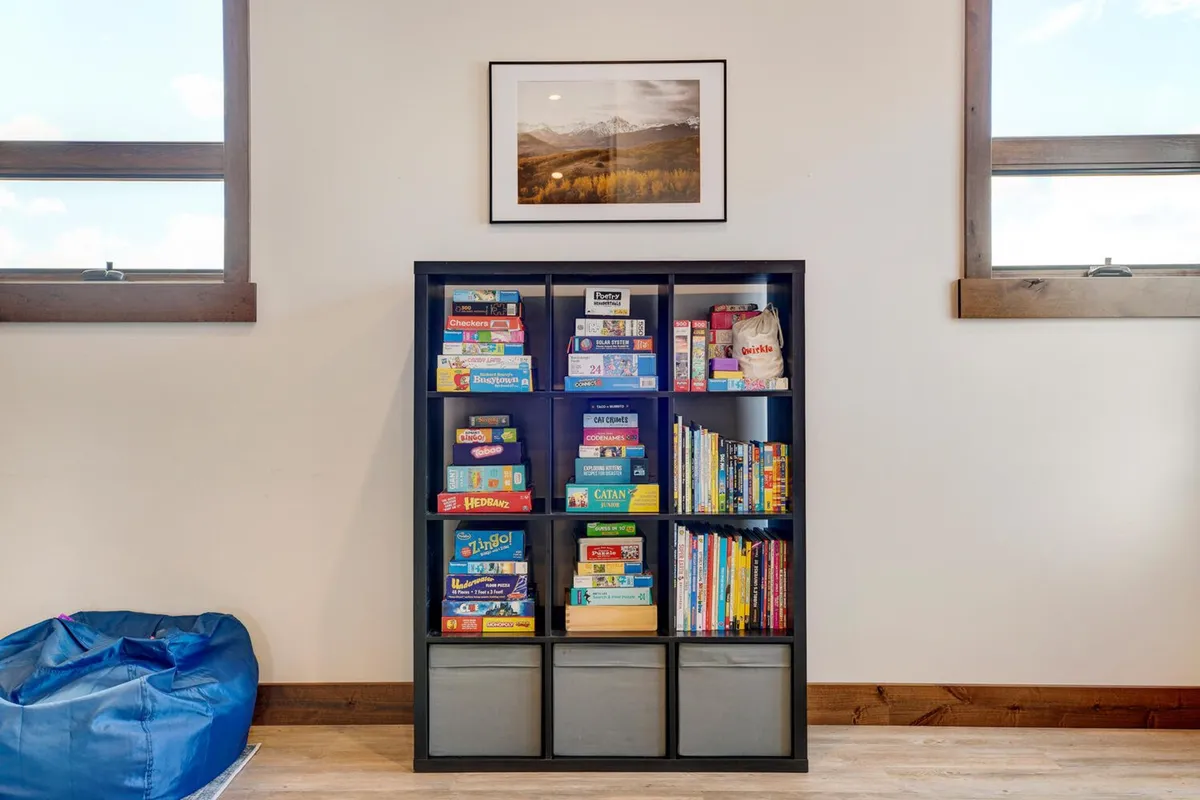 A playful nook featuring a bookshelf filled with books and games, a bean bag chair for lounging, and warm decorative touches. The space is designed for family gatherings, reading, and board games, making it especially welcoming for children.