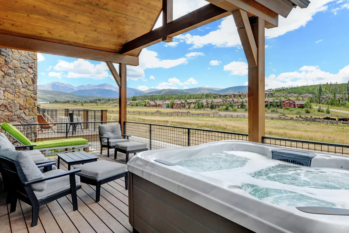 An outdoor scene showcasing a private hot tub on a deck with comfortable seating, all set against a backdrop of mountain views. The tranquil mood suggests relaxation after a day of adventure, with space for socializing or unwinding while watching the sunset.