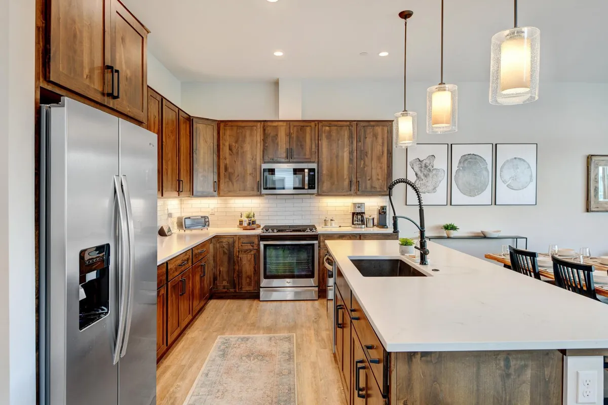 A modern gourmet kitchen with stainless steel appliances, a large kitchen island, custom wooden cabinetry, and pendant lighting overhead. The open layout is designed for cooking, entertaining, and family meals, with decorative elements adding warmth to the space.