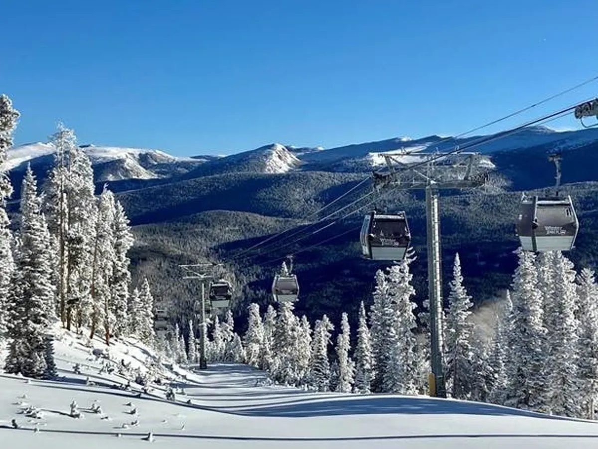 A scenic exterior shot of snow-covered mountains framed by a ski lift and tall pine trees. The environment is invigorating and representative of classic winter mountain activities such as skiing and snowboarding.