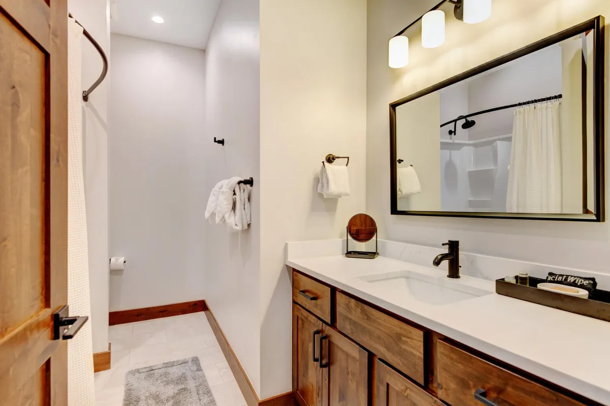 A modern en-suite bathroom with a spacious vanity and mirror, elegant lighting fixtures, and a sleek shower area. The gentle color palette and thoughtful layout create a spa-inspired feel.