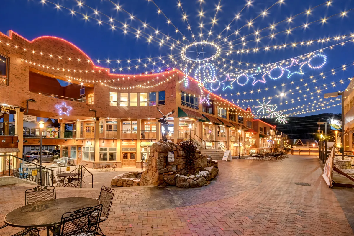 This exterior shot captures a lively streetscape adorned with string lights, decorative stars, and a charming fountain centerpiece. The brick pathway winds through a vibrant area that is ideal for social gatherings, outdoor dining, and evening strolls. Local storefronts and a cozy nighttime ambiance suggest proximity to amenities and entertainment.