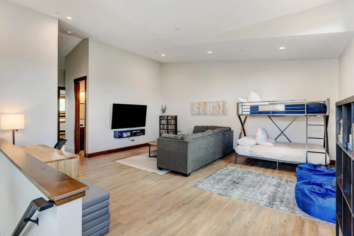 A multi-use family space with a bunk bed, sofa, TV, bookshelf, and a colorful area rug. The room is clearly designed to accommodate kids and teens, with spots for sleepovers, reading, games, and relaxation—all in an inviting, casual atmosphere.