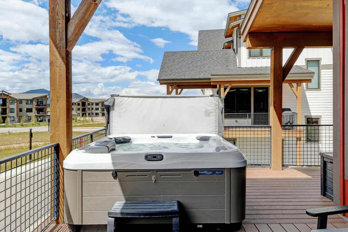 This exterior image features a private hot tub on a deck, overlooking a scenic mountain landscape. The tranquil setting is complemented by the surrounding natural beauty, suggesting a relaxing space to unwind while immersed in the outdoors.