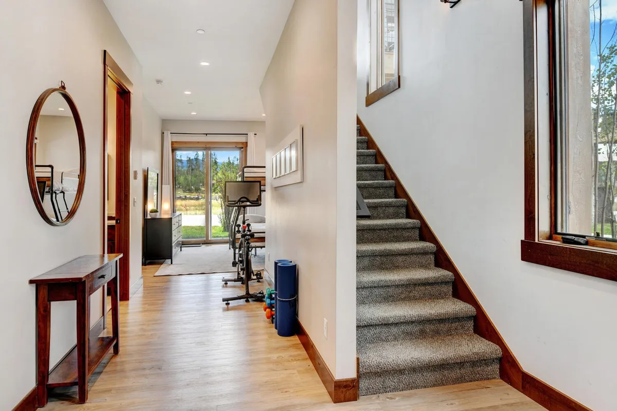 A bright, open interior space featuring a prominent exercise bike near a staircase, framed by large windows that let in ample natural light. A mirror and console table add to the inviting atmosphere, ideal for morning workouts or preparing for an active day.