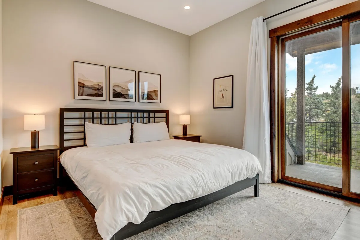 A serene bedroom featuring a comfortable bed with premium bedding, calming wall art, and a sliding door that opens to a private balcony. Soft natural light filters into the space, highlighting the tranquil ambiance designed for restful sleep.