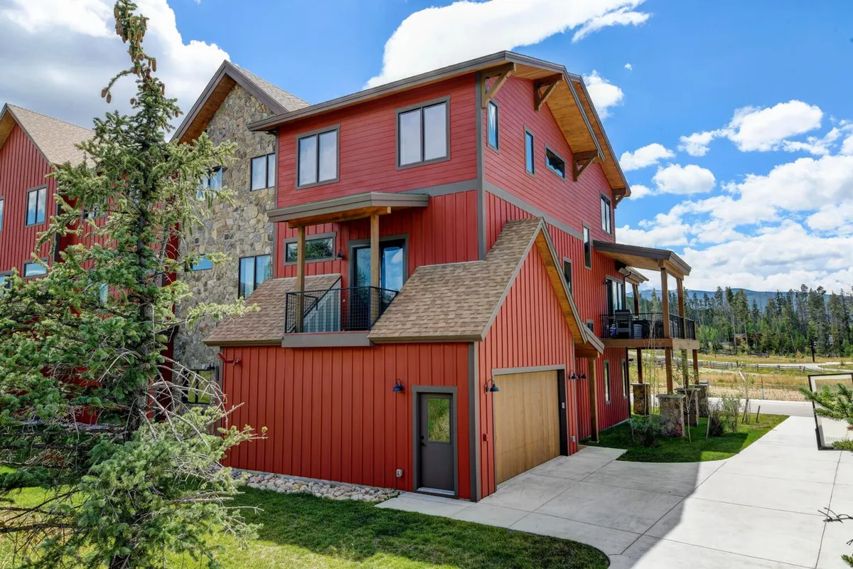 This image features the vibrant red exterior of the house, accented by large windows and a spacious balcony. The scene conveys an inviting and cheerful atmosphere, with outdoor space perfect for family gatherings, morning coffee, or evening barbecues. The surrounding landscape hints at the natural beauty and accessibility to local attractions.